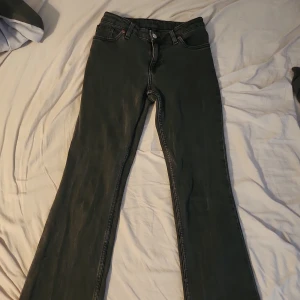 Svarta bootcut jeans med hjärtdetalj - Säljer ett par svarta bootcut jeans med klassisk femficksdesign och bälteshällor. Jeansen har en vit hjärtdetalj på ena bakfickan som ger en personlig touch. Tillverkade i jeansmaterial och har en snygg, något tvättad look. Måtten syns på bild 