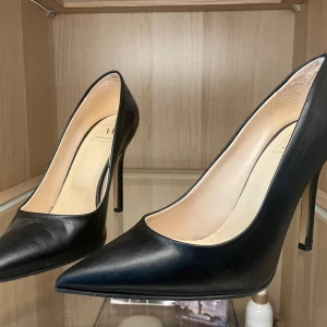 Svarta pumps från Made in Italia - Klassiska svarta pumps från Made in Italia med spetsig tå och hög smal klack. Skorna är tillverkade i slätt skinn och har en elegant, tidlös design som passar perfekt till en dressad look.