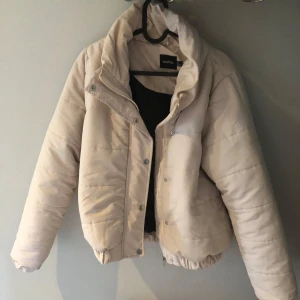 Beige pufferjacka från Boohoo - Snygg beige pufferjacka från Boohoo med hög krage, och en dragkedja och knappar ifram. Använd typ 1-2 gånger gillar den mycket men för kort för mina armar och lite kort för mig överlag.