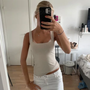 Beige linnetopp med breda axelband - Säljer en stilren beige linnetopp med breda axelband och fyrkantig ringning. Toppen är figurnära och har en enkel, clean look som passar perfekt till jeans eller kjol. Materialet känns mjukt och stretchigt, vilket gör den superbekväm att bära.