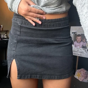 Svart jeanskjol med slits - Säljer en svart kort jeanskjol med snygg slits på ena sidan. Kjolen har en klassisk femficksmodell och dragkedja bak. Perfekt att matcha med en stickad tröja eller crop top för en chill look.
