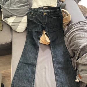 Lågmidjade  - Snygga mörkblå jeans från Vavell med bootcut passform. Bakfickorna har dragkedjor och är dekorerade med blingade bokstäver i strass. Klassiska gula sömmar och coola detaljer som ger jeansen en unik vibe. Perfekta för dig som vill sticka ut lite extra. Lågmidjade, står XL men är verkligen inte de. Passar nån som har 38 i strl och 170.