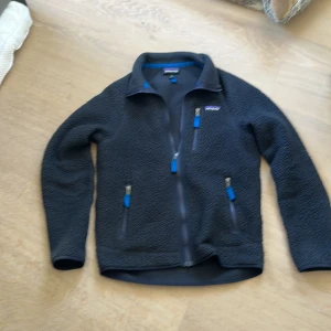 Mörkblå fleecejacka från Patagonia XS -  mörkblå fleecejacka från Patagonia i storlek XS. Jackan har hel dragkedja, tre fickor med blå detaljer och hög krage. Perfekt för lager-på-lager och chill dagar. Klassisk Patagonia-logga på bröstet och mjukt fleece-material. skriv vid funderingar 👍