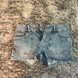 Ljusblå jeansshorts från Lindex - Snygga ljusblå jeansshorts från Lindex med dubbla knappar och dragkedja framtill. Shortsen har stora fickor och broderade hjärtan på bakfickorna för en extra cool detalj. Perfekta för varma dagar och chill häng. Endast använda ett fåtal gånger!