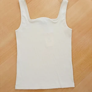 Vit ribbad linnetopp  - Säljer en stilren vit ribbad linnetopp  i storlek L. Toppen har breda axelband och en snygg, något vågig kant vid urringningen. Perfekt att matcha med jeans eller kjol för en clean look.