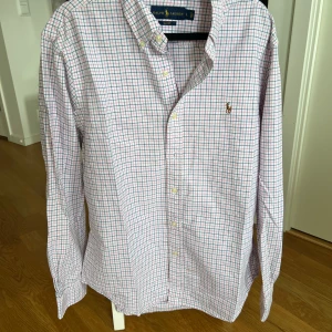 Rutig skjorta från Ralph Lauren - Säljer en stilren rutig skjorta från Ralph Lauren i slim fit. Skjortan har ett klassiskt rutmönster i blått och rosa på vit bakgrund. Den är i storlek L men passar som en M 