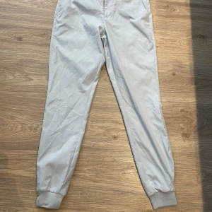 Grå byxor från Puma golf - Snygga grå byxor från Puma golf med elastiska muddar vid bensluten. Byxorna har en stilren design med två bakfickor och en bekväm passform. Perfekta för en avslappnad stil.