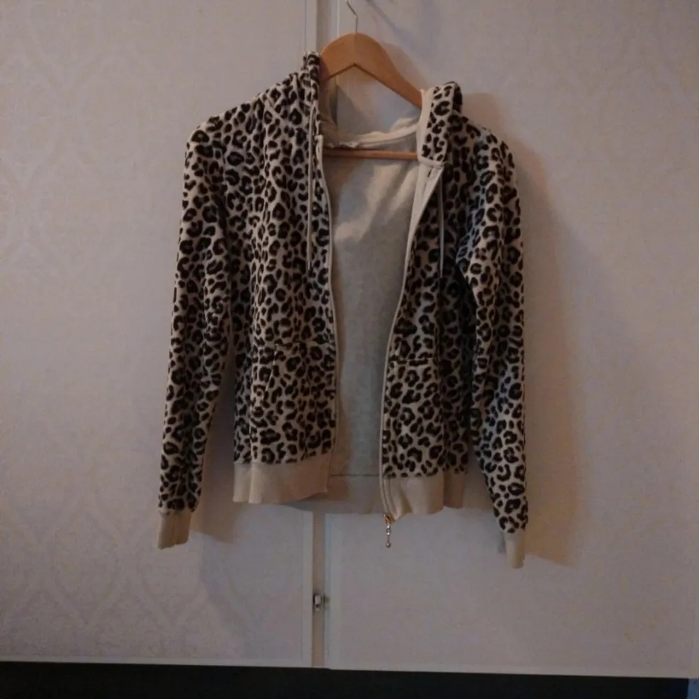 Mysig hoodie med leopardmönster i beige och bruna toner. Jackan har huva, dragkedja framtill och ribbade muddar vid ärmslut och nederkant. Perfekt för dig som gillar djurmönster och vill ha en cool och bekväm stil.. Takit.