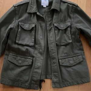 Grön utilityjacka från Gina Tricot - Säljer en grön utilityjacka från Gina Tricot med fyra stora fickor framtill och klassisk krage. Jackan har lång ärm och knäppning med knappar. Perfekt för dig som gillar en avslappnad och cool stil. Väldigt gott skick! 