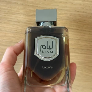 Parfym Lattafa Liam Grey  - Upptäck Liam Grey från Lattafa, en elegant doft med toppnoter av kardemumma, fikon och svart te. Mellannoterna består av iris, vetiver och labdanum, medan basnoterna bjuder på vanilj, sandelträ, tonka och patchouli. Perfekt för den som söker en sofistikerad och unik doftupplevelse. 100 ml, enbart testad, kommer i originalkartongen. 