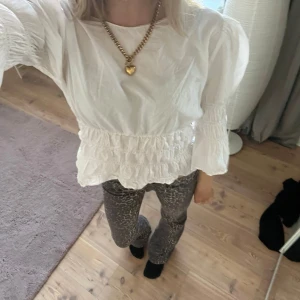 Vit blus med volangdetaljer - Säljer en söt vit blus med volangdetaljer och trekvartsärmar. Blusen har en elastisk midja som ger en fin passform. Perfekt för en stilren look.