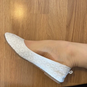 Vita ballerinaskor med blommigt broderi - Säljer ett par vita ballerinaskor med fint blommigt broderi och liten rosett bak. Skorna har rund tå och är perfekta för vår och sommar.