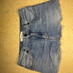 Blå jeanskjol från Mango - Snygga blå jeanskjol från Mango med råa, fransiga kanter och klassisk femficksdesign. Kjolen har , knapp och dragkedja framtill samt en avslappnad passform. Perfekta för varma dagar💖