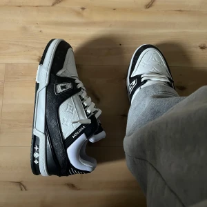 Lv trainers - Säljer ett par snygga Louis Vuitton sneakers i svart och vitt med tydliga LV-detaljer och mönster på ovandelen. Skorna har snörning, rund tå och platt sula. Perfekta för dig som vill sticka ut med exklusiva och trendiga sneakers.