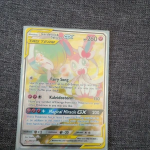 Pokémonkort Gardevoir & Sylveon GX Tag Team - Säljer ett holografiskt Pokémonkort med Gardevoir & Sylveon GX Tag Team. Kortet har färgglad design med rosa, blå och gula detaljer. HP 260 och flera attacker som Fairy Song, Kaleidostorm och Magical Miracle GX. Perfekt för samlare eller Pokémon TCG-spelare.