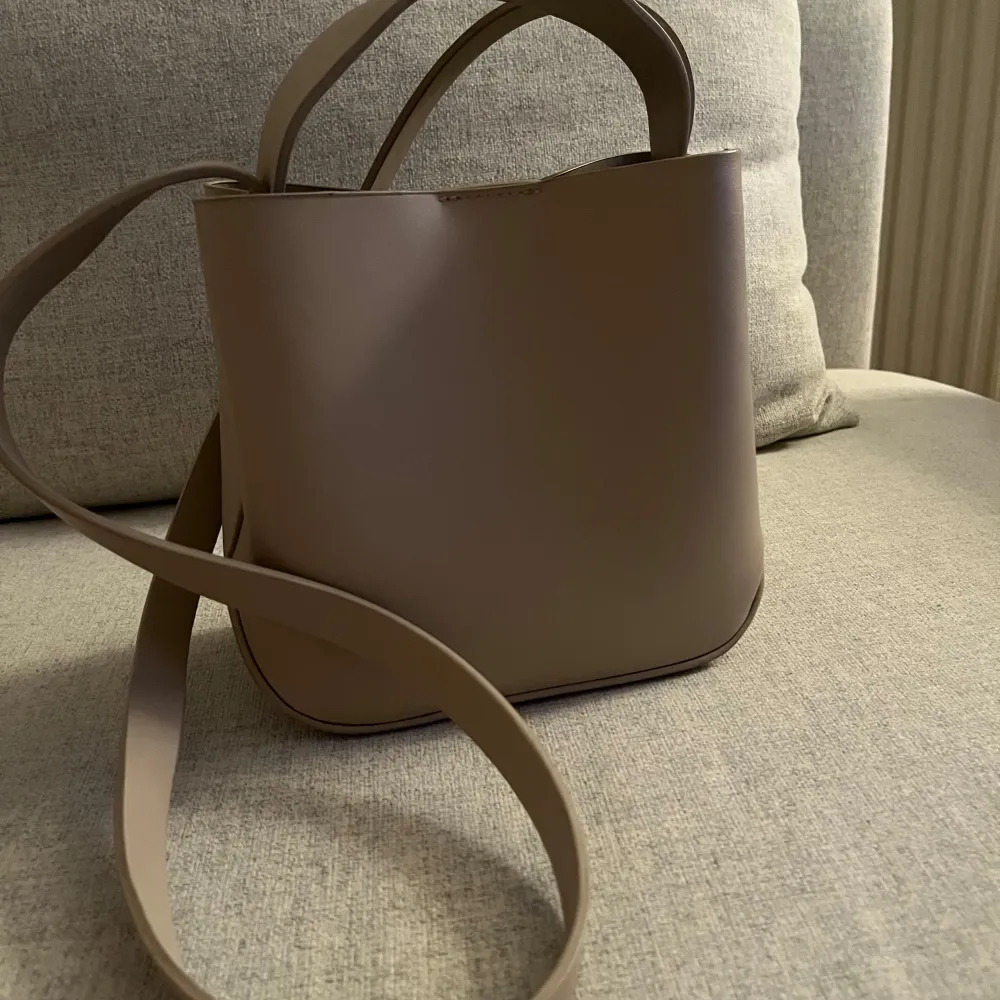 Säljer en stilren beige axelväska med minimalistisk design. Väskan har både korta handtag och en lång axelrem samt ett innerfack med dragkedja och magnetlås. Perfekt för dig som gillar enkel och modern stil.. Laukut & Käsilaukut.