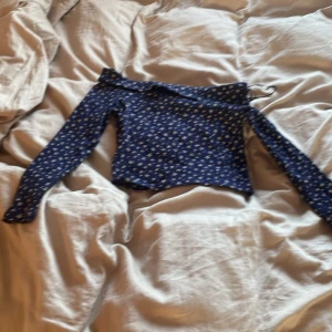 Blå blommig topp från H&M - Säljer en söt blå topp från H&M med vita blommor. Toppen har långa ärmar och en offshoulder-design som ger en trendig look. Perfekt för vårens och sommarens dagar! 🌸