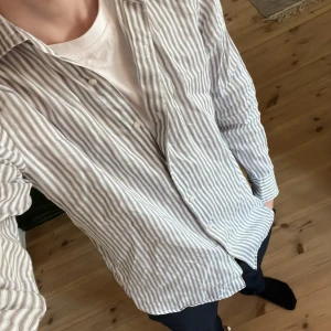 Randig skjorta från Massimo Dutti - Säljer en stilren randig skjorta från Massimo Dutti i blått, vitt och beige. Skjortan är långärmad med knappar framtill och är tillverkad i linne. Den är luftig och perfekt för sommaren!⛱️⛱️⛱️Storleken är S och den skulle passa någon mellan 175-185 cm! Skriv gärna om ni har funderingar🤗