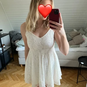 Vit spetsklänning - Säljer en söt vit spetsklänning med v-ringad design. Klänningen är ärmlös och har en kort längd som passar perfekt för sommarens festligheter. Den har en fin passform som framhäver figuren. Aldrig använd!