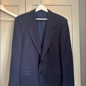 Mörkblå kavaj från Widengrens - Elegant mörkblå kavaj från Widengrens, tillverkad i ren ull. Klassisk design med två knappar framtill och fickor. Perfekt för formella tillfällen.