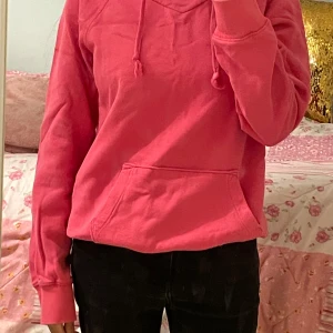 Rosa hoodie med ficka - Säljer en enkel och snygg rosa hoodie med huva och dragsnören. Tröjan har en stor magficka framtill och är tillverkad i mjukt material. Perfekt för en avslappnad stil.
