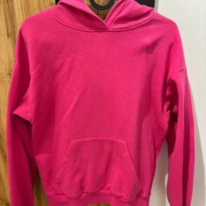 Rosa hoodie från H&M - Säljer en enkel och snygg rosa hoodie från H&M. Tröjan har huva, lång ärm och en stor magficka framtill. Perfekt för dig som gillar en färgstark och bekväm stil.