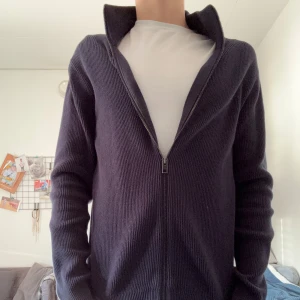 Mörkblå ribbad kofta från Kappahl - Säljer en mörkblå ribbad kofta från Kappahl i storlek S. Koftan har dragkedja framtill och hög krage, perfekt för lager-på-lager. Enkel och stilren design som passar till mycket.