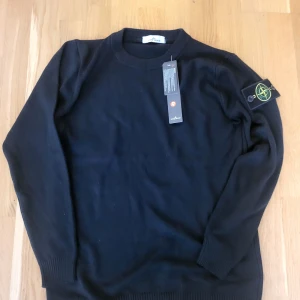 Svart stickad tröja från Stone Island - Säljer en svart stickad tröja från Stone Island med klassisk rund halsringning och ikonisk logotyp på ärmen. Tröjan har långa ärmar och ribbade muddar. Perfekt för dig som gillar stilrena och exklusiva plagg.