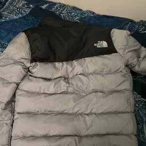 Säljer en grå och svart pufferjacka från The North Face. Jackan har lång ärm, dragkedja framtill och två fickor med dragkedja. Perfekt för kyligare dagar och riktigt skön att bära.