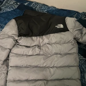 Grå och svart pufferjacka från The North Face - Säljer en grå och svart pufferjacka från The North Face. Jackan har lång ärm, dragkedja framtill och två fickor med dragkedja. Perfekt för kyligare dagar och riktigt skön att bära.