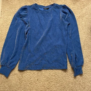 Blå glittrig tröja från LMTD - Snygg blå tröja från LMTD med glittrande detaljer. Tröjan har långa ärmar och en rund halsringning. Perfekt för att lägga till lite glitter i vardagen. Passar ungdomar i storlek 13-14 år. har aldrig använt fick i födelsedagspresent
