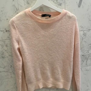 Ljusrosa stickad tröja från Mango i ullmaterial - Mysig ljusrosa stickad tröja från Vero Moda. Perfekt för kyliga dagar med sin mjuka och bekväma passform. Tröjan har långa ärmar och en rund halsringning.