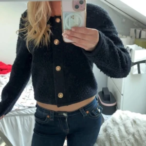 Marinblå teddyjacka med knappar - Säljer en mysig marinblå teddyjacka med stora guldknappar framtill. Jackan är croppad och har långa ärmar, perfekt för en trendig look. Passar bra till både jeans och kjol.