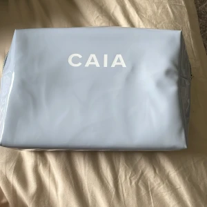 Ljusblå necessär från CAIA - Säljer en ljusblå necessär från CAIA med vitt tryck på framsidan. Väskan har dragkedja och är rymlig med lila insida. Perfekt för smink eller andra småsaker. Enkel och stilren design. Säljer då jag fick den i födelsedagspresent för något år sedan och jag inte använder den längre. Säljs inte längre på hemsidan. Inga märken eller skador.