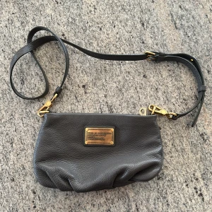 Svart axelväska från Marc by Marc Jacobs - Snygg svart axelväska i skinn från Marc by Marc Jacobs med justerbar rem och guldfärgade metalldetaljer. Väskan har dragkedja och en metallplatta framtill med logga. Fodret är mönstrat med stora bokstäver. Man får 5% RABATT när följer NordqvistFashionCloset på Instagram samt här på plick!!😊Mvh Wilgot