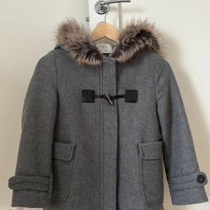 Grå kappa med pälsdetalj från Zara - Snygg grå kappa från Zara med en mysig pälskantad huva. Jackan har en stilren design med knäppning framtill och praktiska fickor. Perfekt för kyliga dagar.köpte jackan för 400kr säljer nu för 200 vi kan diskutera på priset. 