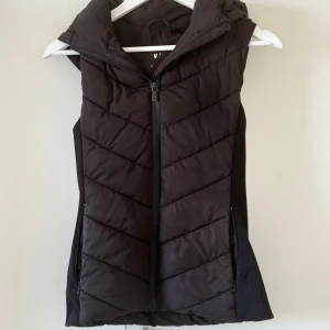 Svart quiltad dunväst från zara - Säljer nu min jätte snygga svart dunväst med dragkedja och huva från Zara. Den sitter tajt och passar xss-s💕