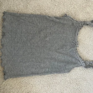 Grå ribbad linnetopp från H&M - Säljer en grå ribbad linnetopp från H&M med spetsdetaljer och en liten rosett vid halsringningen. Super söt! Knappt använd. 🩶