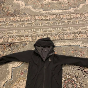 Svart vindjacka från Haglöfs, M - Svart vindjacka från Haglöfs i storlek M. Jackan har huva, hel dragkedja framtill och två sidofickor. Tillverkad i lätt och slitstark polyester, perfekt för blåsiga dagar. Köpt för cirka 1200 behövs ej mer så säljer lågt pris. Som ny inga fläckar.