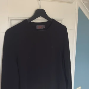 Svart merinoulltröja från Morris - Svart långärmad tröja från Morris i 100% merinoull. Klassisk rund hals och diskret Morris-logga broderad på bröstet. Perfekt för dig som gillar stilrena och enkla plagg med lyxig känsla. Snygg passform och mjukt material som känns skönt mot huden.