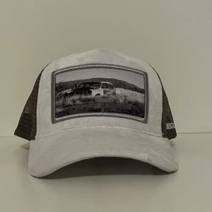 Vit och grå keps med bilmotiv - Snygg keps i vit och grå mesh med ett stort svartvitt tryck av en bil på framsidan. Framsidan är i mjukt tyg och baksidan i ventilerande mesh. Perfekt för dig som gillar coola motiv och streetstyle.