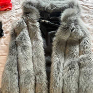 Grå fluffig pälsväst - Säljer en superfluffig grå pälsväst med bred krage och snyggt fall. Västen har en lyxig känsla och är perfekt för att höja din outfit. Pälsen är långhårig och ger en cool statement-look.