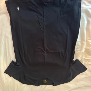 Svart t-shirt från Polo Ralph Lauren - Svart t-shirt från Polo Ralph Lauren med klassisk vit broderad logga på bröstet. T-shirten har rund hals och korta ärmar, tillverkad i mjuk bomull som känns skön mot huden. Perfekt för en clean och enkel stil. Nästan ny och helt fräsch.