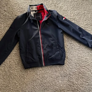 Tommy Hilfiger vindjacka  - Marinblå vindjacka från Tommy Hilfiger. Jackan är vattenavvisande och i ett riktigt bra skick.                          Vid frågor är det bara att höra av sig