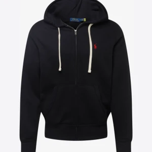 Svart hoodie från Polo Ralph Lauren - Snygg svart hoodie från Polo Ralph Lauren med vit snörning och dragkedja framtill. Klassisk röd logga broderad på bröstet, huva och stora fickor. Den är inte trasig på något sätt. Köpte den för 2200 säljer för 899kr. Skriv för fler bilder på!