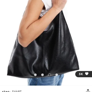 Svart axelväska från asos - Stilren svart axelväska med mjuk, slät yta i skinnimitation. Väskan har en enkel, rymlig design med bred axelrem och lätt v-formad öppning. Perfekt för att bära med sig allt man behöver under dagen och passar till de flesta outfits. Hör av er om ni har prisförslag eller nån fråga!💕
