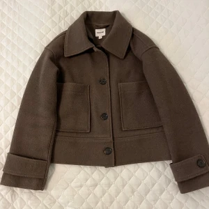 Brun overshirt jacka från Kappahl - Snygg brun overshirt jacka från Kappahl i storlek XS. Jackan har en boxig passform, stora framfickor och knappar framtill samt på ärmsluten. Materialet är ullblandning som ger en mjuk och varm känsla. Perfekt till hösten!