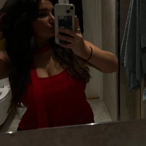 Röd ärmlös topp med scarfdetalj - Säljer en snygg röd topp med ärmlös design och en matchande scarfdetalj runt halsen. Toppen har en rak och figurnära passform som framhäver siluetten. Perfekt för dig som vill sticka ut med en enkel men cool look.