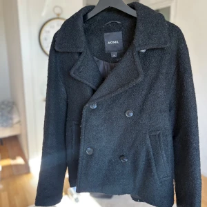 Svart kort kappa från Monki - Säljer en svart kort kappa från Monki med dubbelknäppning och bred krage. Jackan har en två fickor fram. 