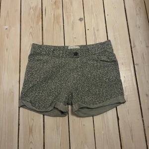 Grå leopardmönstrade shorts - Snygga grå shorts med leopardmönster och uppvikta benslut. De har skärphällor och både fram- och bakfickor. Perfekta för dig som vill sticka ut med ett coolt mönster och avslappnad stil. 